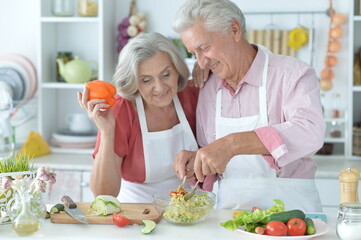 happy senior couple making salad together at kitchen