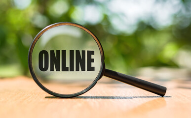 Magnifying glass with text ONLINE on wooden table and green background.