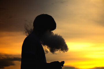 Man smoke electronic cigarette outdoor on beautiful sky background during sunset.