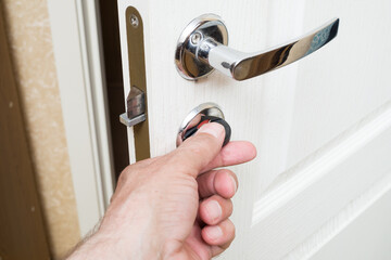 Worker installing or repairing new lock and door knob with screwdriver. Locksmith repair or install the door lock in house.