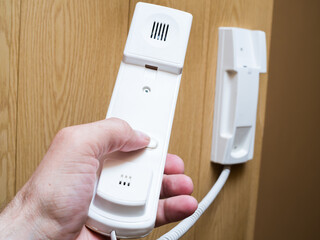 Concept of house security. Vertical cropped view of woman hand holds the intercom receiver headset, standing in apartment hall