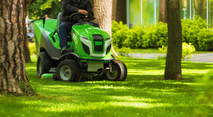 Professional worker trimming green grass with lawn mower m tractor in the park. - obrazy, fototapety, plakaty