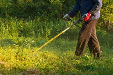 Gardener mows a green lawn with a hand-held lawn mower.