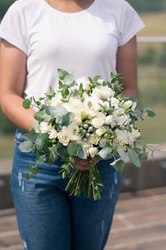 Florist hands holding modern bridal bouquet of white flowers and greenery. Wedding bouquet composed of roses, freesia, lisianthus, brunia and eucalyptus.
