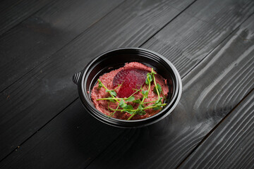 Beetroot hummus garnished with herbs in black bowl on dark wooden table