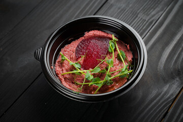 Beetroot hummus garnished with herbs in black bowl on dark wooden table