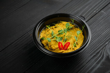 Hummus garnished with peppers chilli and herbs in black plate on dark wooden table.