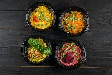 Hummus garnished peppers, chili, beet and herbs in black bowl on dark wooden table. Hummus assortment