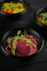 Hummus garnished peppers, chili, beet and herbs in black bowl on dark wooden table. Hummus assortment