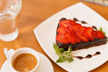 Chocolate cake, brownie with strawberries and mint, espresso, glass of water on a wooden table