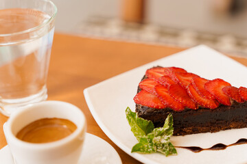 Chocolate cake, brownie with strawberries and mint, espresso, glass of water on a wooden table