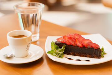 Chocolate cake, brownie with strawberries and mint, espresso, glass of water on a wooden table