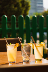 Cocktails with lemon and mint in glasses with tube on a wooden table against the background of a restaurant. Cold summer lemonade