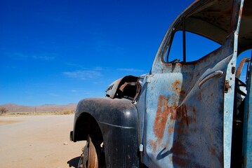 Left side of an old rusty car wreck in the Namibian desert on a sunny day with blue sky and few...