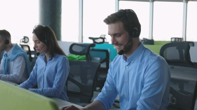 Call center worker accompanied by his team. Smiling customer support operator at work.