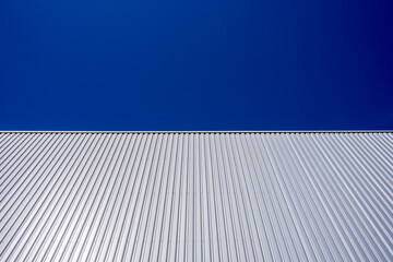 Fototapeta na wymiar View upwards to the facade of a warehouse with a cladding of silver corrugated aluminum sheet. Corrugated iron sheet, aluminum Facade of a warehouse as background texture