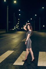 A woman in a short dress on a pedestrian crossing in the lights of the night city. Empty night road. vertical