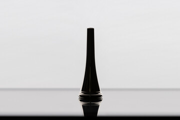 A silhouette of a French horn mouthpiece on a reflective surface with a white background