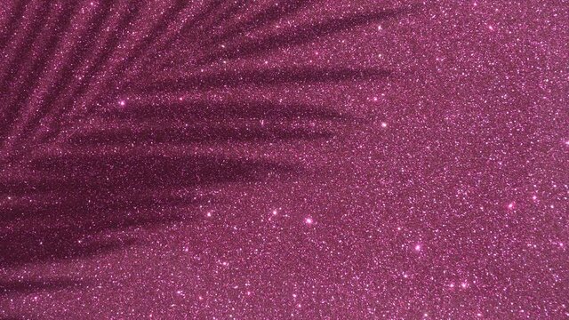 Shadows from a palm tree on a pink glitter sparkling shining background. Minimal art, glamor, vacation, summer, party concept.