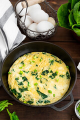 Omelette with spinach, green onions and feta cheese in a cast-iron frying pan on a dark wooden background. Healthy breakfast. Rustic style. Copy space.