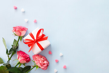 Pink roses flowers and present gift on blue background. Minimalistic composition for Valentine's or Mothers day and holidays. Greeting card concept.