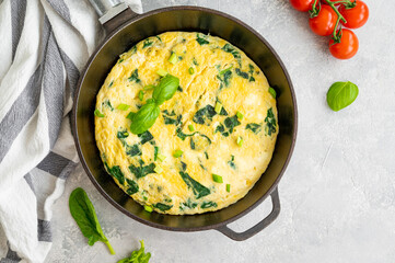 Omelette with spinach, green onions and feta cheese in a cast-iron frying pan on a gray concrete background. Healthy breakfast. Top view, copy space.