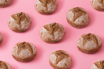 Bread buns pattern on pink background, creative colorful pattern with small round dark bread, raw grain