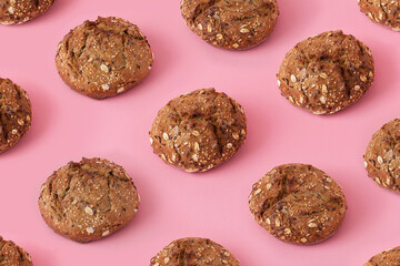 Brown bread buns with seeds on pink background, creative colorful pattern with small round dark bread