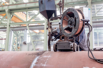 Welder operator is welding to pipe with submerged arc welding (SAW) method in the workshop. The process requires a continuously fed consumable solid or tubular (metal cored) electrode.