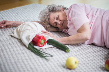 Old lady lying on the floor next to shopping bag with vegetables