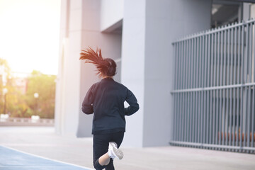 Back of Asian Beautiful Young woman black suit with happy running or jogging on blue running track in the day time. exercise, training, fitness, workout, sport, lifestyle and healthy concept.