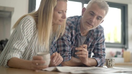 Middle-aged couple in kitchen reading newspaper - Powered by Adobe