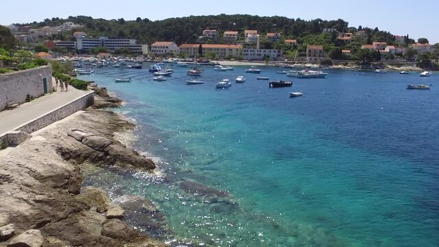 Une vid&eacute;o a&eacute;rienne avant au dessus d'une eau turquoise et limpide dans une destination paradisiaque m&eacute;diterran&eacute;enne. Passage proche des rochers et vue sur la ville 
