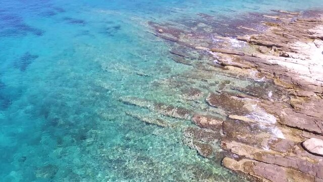Une vid&eacute;o a&eacute;rienne avant au dessus d'une eau turquoise et limpide dans une destination paradisiaque m&eacute;diterran&eacute;enne. Passage proche des rochers et vue sur la ville d'une ile
