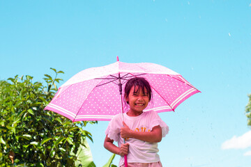 Asian little girl standing with an umbrella with joyfulness while it is raining and sunny during the day.