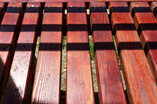 Red stained pine board deck in harsh sunlight , shadows crossing the image.
