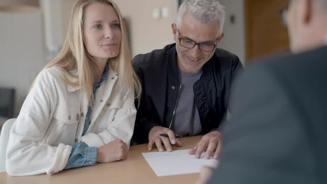 Middle-aged couple with real-estate agent signing contrat 