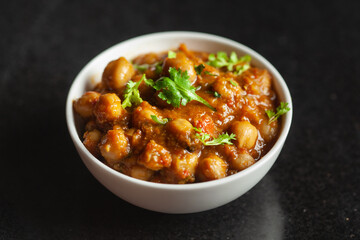 Chickpeas masala (Spicy chola or chhole curry)  garnished with fresh green coriander and ingredients. Served in a ceramic bowl. An Classic Indian typical Panjabi street food.  