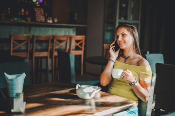 portrait of young teenager brunette girl with long hair sitting indoor in urban cafe and use her smartphone