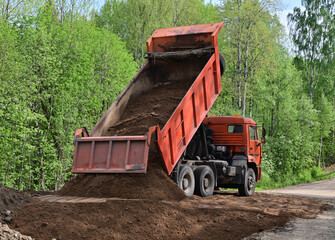 A truck unloads sand on a country road to level and repair the pavement