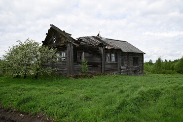 An old abandoned one-story hut with a collapsed roof. The windows are broken in places