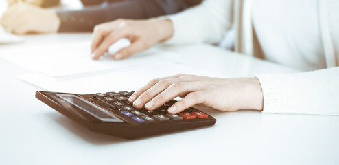 Accountant checking financial statement or counting by calculator income for tax form, hands closeup. Business woman sitting and working with colleague at the desk in office. Tax and Audit concept