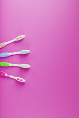 Four toothbrushes on a pink background in a row.