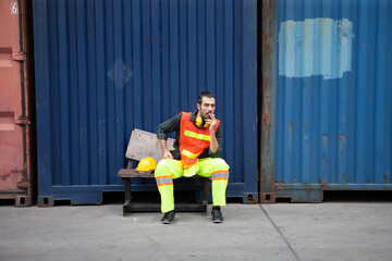 Plakat harbor worker take a break sitting and smoking cigarette on Containers box background at warehouse logistic in Cargo.