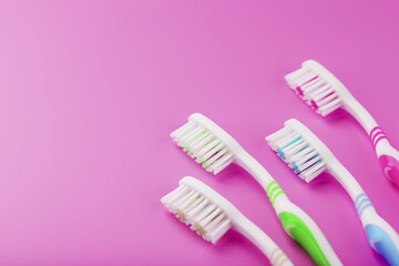 Four toothbrushes on a pink background in a row.