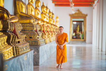 Fototapeta premium Monk walking down the hallway with buda statues around him