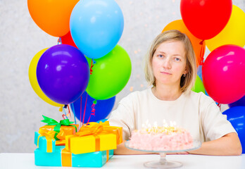 Fototapeta na wymiar Woman with candles on a birthday cake on a background of gifts and balloons