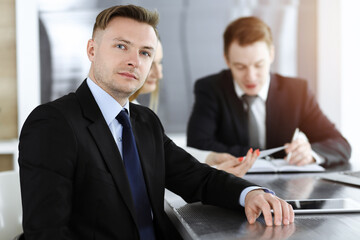 Businessman headshot at meeting in sunny office. Unknown entrepreneur sitting with colleagues at the background