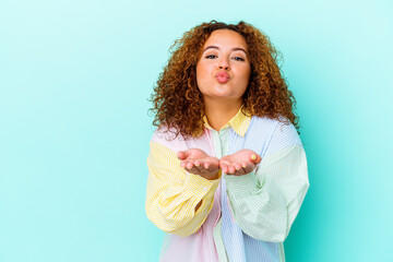 Young latin curvy woman isolated on blue background folding lips and holding palms to send air kiss.