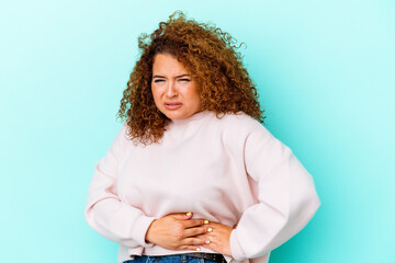 Young latin curvy woman isolated on blue background having a liver pain, stomach ache.